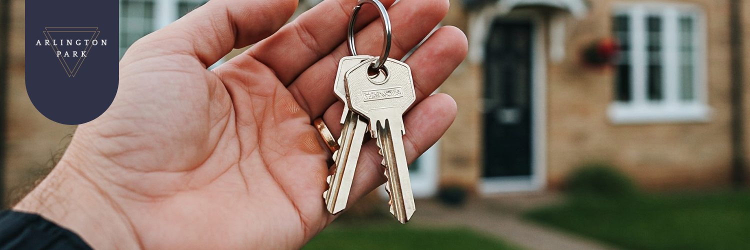 Close-up of a hand holding new house keys with a blurred home in the background, representing the excitement of buying property.